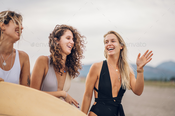 Portrait of a three attractive woman friends walking with surfboard on a beach - Stock Photo - Images