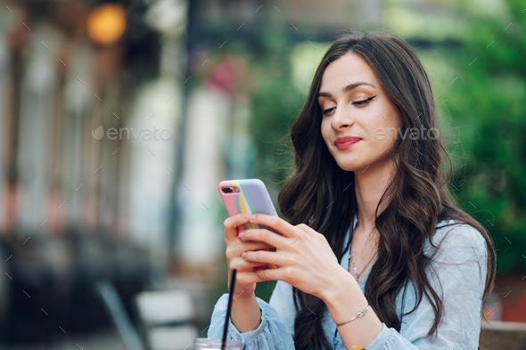 Portrait of a beautiful woman sitting in a street cafe and using a smartphone - Stock Photo - Images