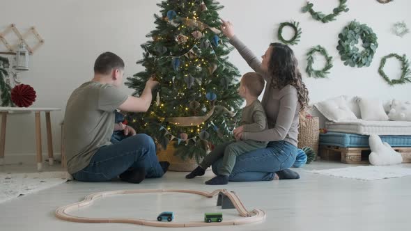 Young Family of Four Sitting Near Christmas Tree alt