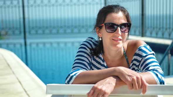 Beautiful European Woman in Sunglasses Lying on Deck Chair with Arms Crossed Enjoying Sun alt