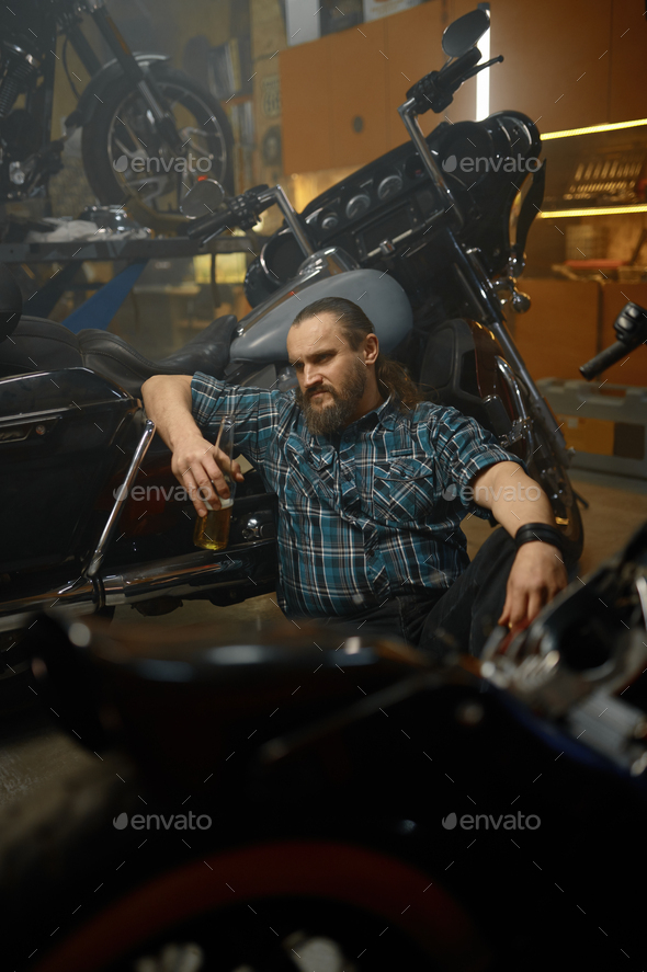 Serious biker sitting on floor and thinking searching way to repair motorcycle - Stock Photo - Images
