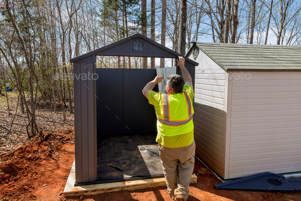 An individual assembles together a plastic vinyl storage shed for his backyard