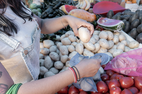 A young Hispanic woman is buying potatoes in a street market using a reusable bag