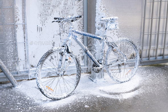 Washing a bicycle with a foam jet at a car wash. The bike is covered with foam. Bicycle maintenance