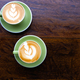 Two green cups of cappuccino with latte art on wooden table. - PhotoDune Item for Sale