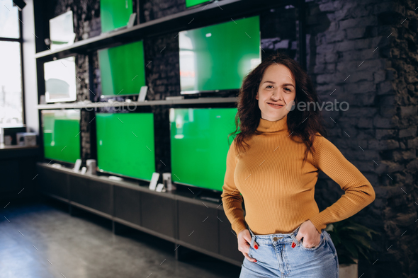 a woman in an electronics store chooses a TV on the background of TVs with a green screen