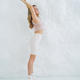 Young smiling blonde woman in sportswear doing stretching on background of white wall - PhotoDune Item for Sale