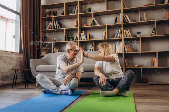 Sportive senior couple doing fitness and relaxation exercises at home ...