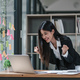 Happy young creative Asian woman working office desk feeling excitement raising her arms up as - PhotoDune Item for Sale