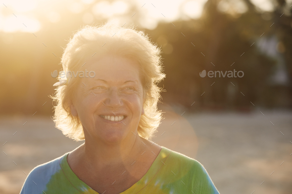Happy senior woman on beach in tropical destination at sunset - Stock Photo - Images