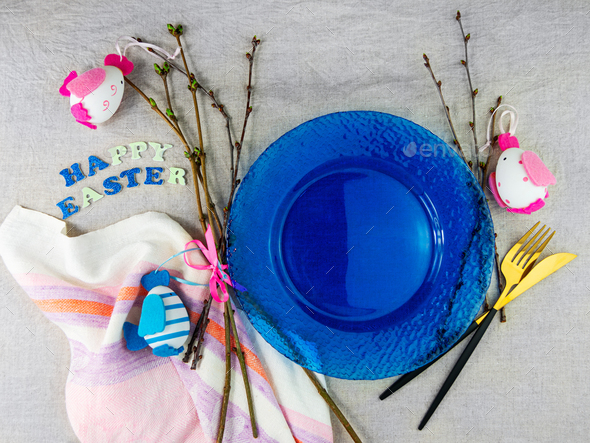 Happy Easter table setting blue glass plate fork knife tree branches on linen cloth. Festive menu