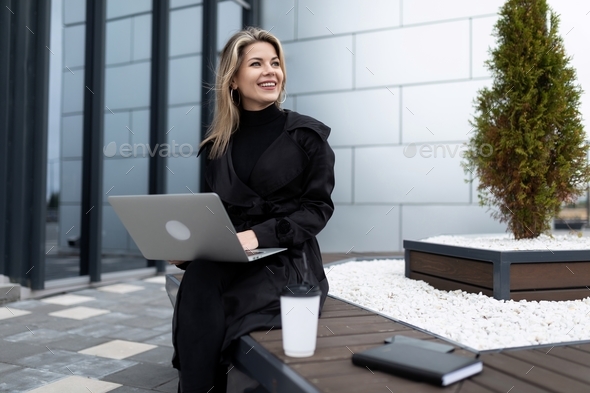 stylish business woman during a break drinking coffee on the street with a laptop in her hands - Stock Photo - Images