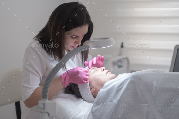 cosmetologist examines client skin through magnifying lamp during a professional facial treatment.