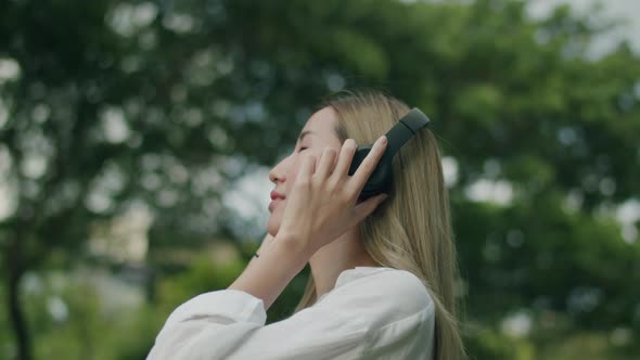 Asian women enjoy the breeze outdoors and have fun wearing headphones listening to music.