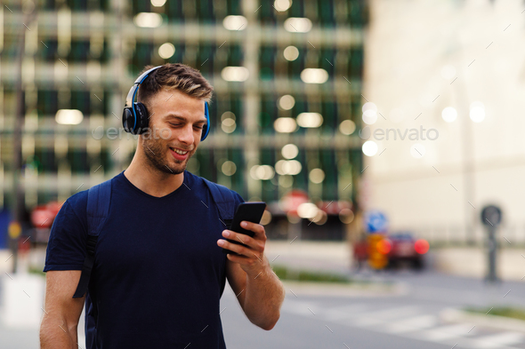 Young sport man walking in the city and listens to music via