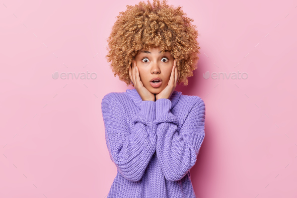 Photo Of Shocked Impressed Curly Haired Woman Keeps Hands On Cheeks