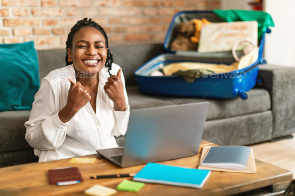 Overjoyed black woman gesturing YES, buying hot tour at web travel agency via laptop from home