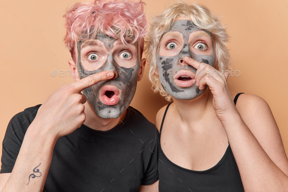 Photo of shocked stunned woman and man touch nose apply facial clay mask for skin care hold breath
