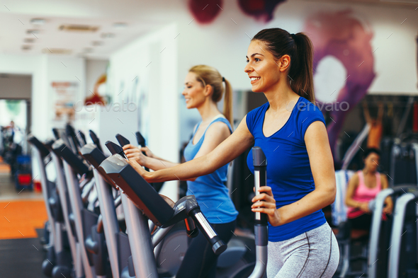 Two young woman exercising on stepper machine at gym