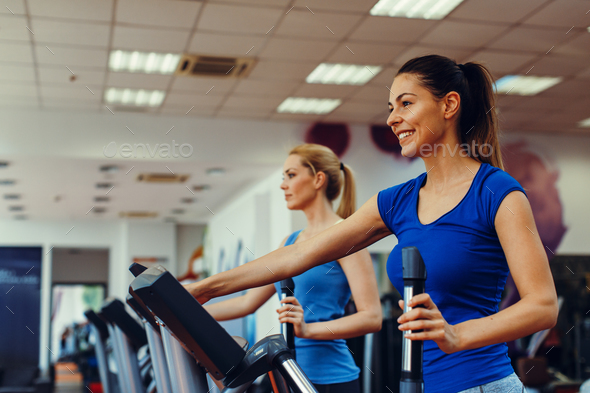 Two young woman exercising on stepper machine at gym