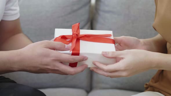 Close up hands Asian man giving Christmas box to girlfriend while sitting on the sofa at home.