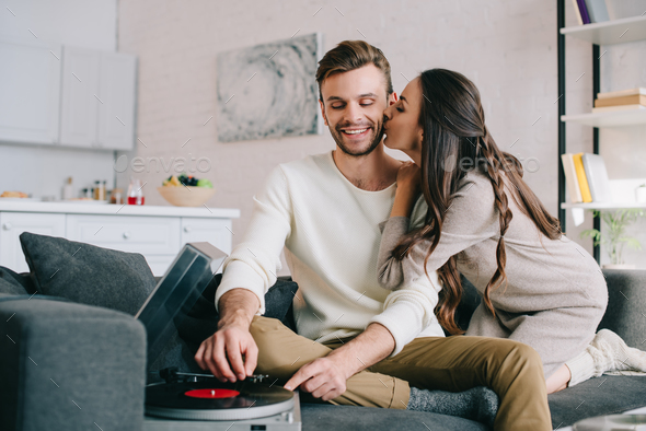 happy young couple listening music with vinyl record player and cuddling at home