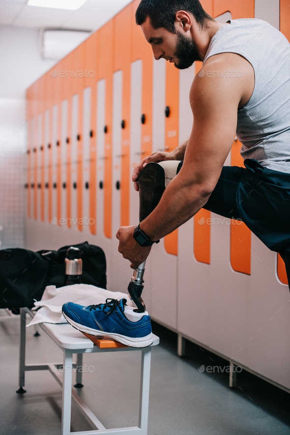 handsome young sportsman putting on artificial leg at gym changing room