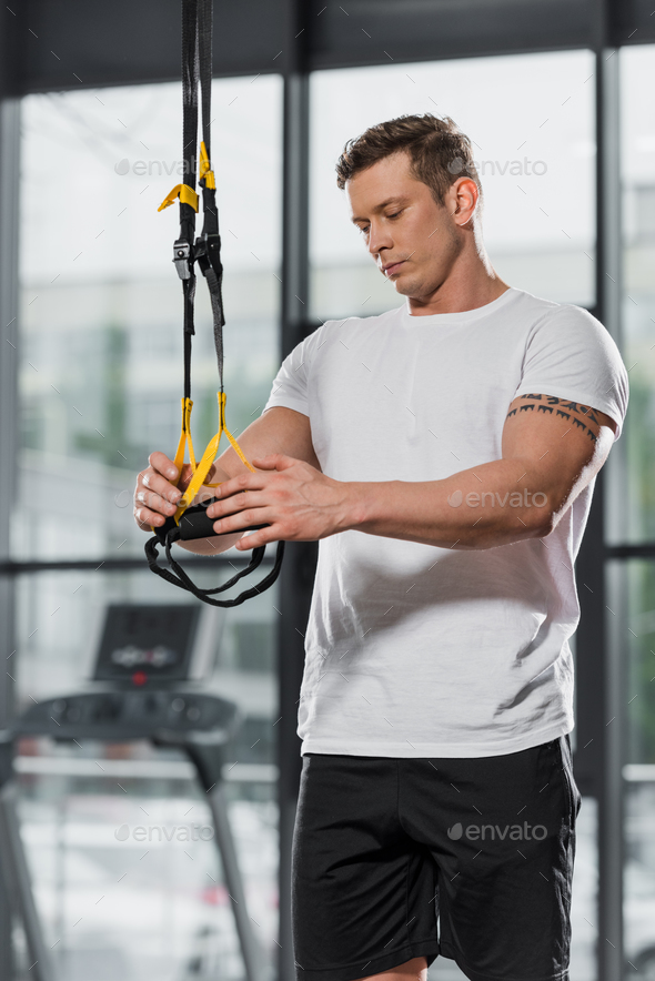 handsome athletic bodybuilder holding suspension straps in gym Stock