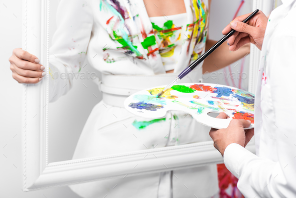 close up of adult man drawing on white clothes with paintbrush while woman holding frame