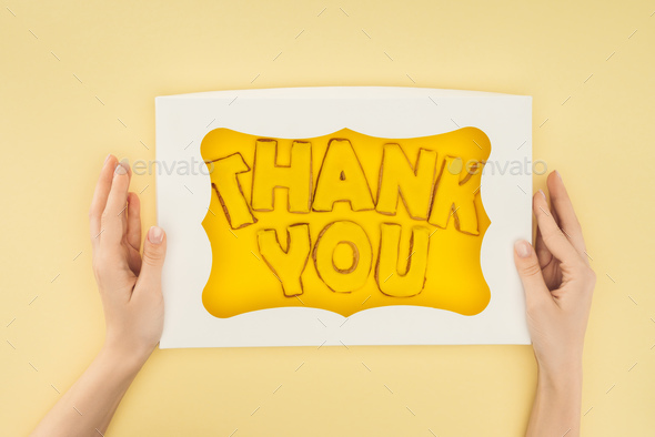 cropped person holding square-shaped cake in box with thank you lettering isolated on yellow