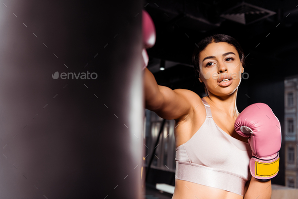 Attractive strong girl in pink boxing gloves practicing boxing in gym