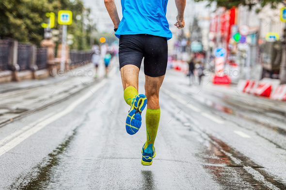 back male athlete in compression socks running marathon in city