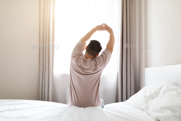 Well-rested Indian Guy in Pajamas Stretching in Bed Stock Photo