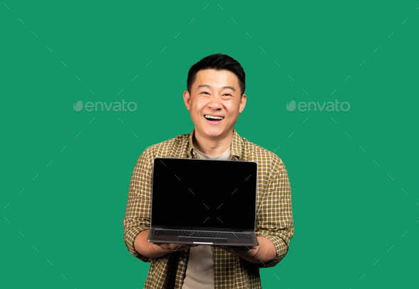 Happy asian middle aged man showing laptop computer blank screen, recommending great website, green