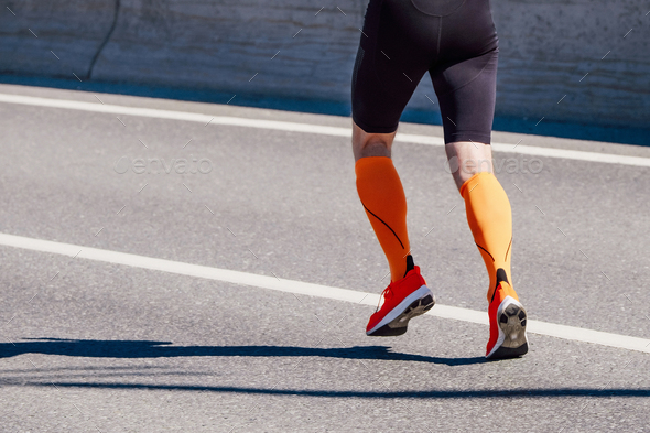 legs male runner in orange compression socks and black tights run race on road