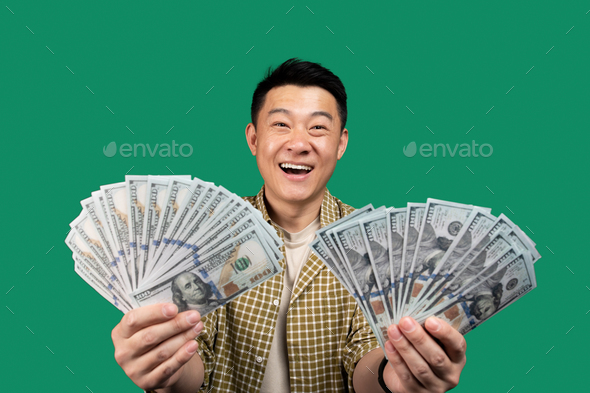 Joyful asian middle aged man holding bunches of money, celebrating success and lottery win over