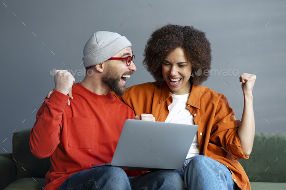 Overjoyed friends using laptop , watching football game, sports betting, win money sitting at home