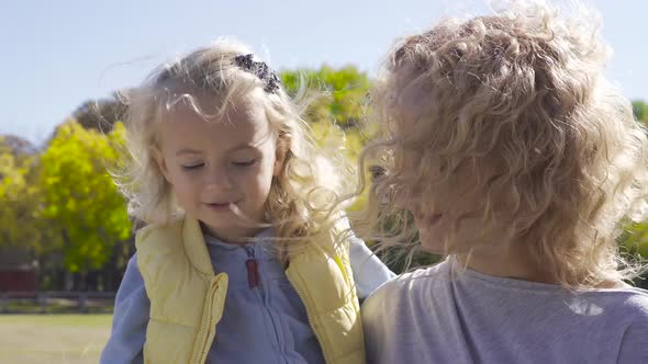 Blond Woman with Curly Hair Holding Little Pretty Caucasian Girl on Hands alt