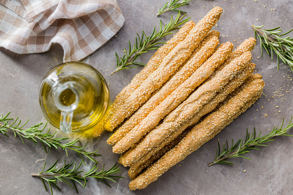 Italian grissini bread sticks with sesame seeds and rosemary on kitchen  table. Top view. Stock Photo by jirkaejc