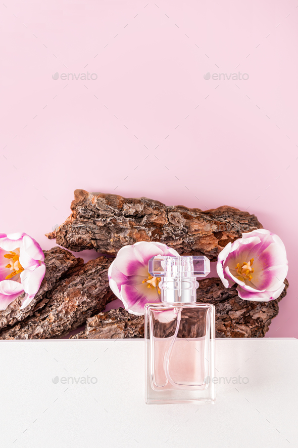 a bottle of cosmetic spray or toilet water lies on a white podium and parts of the bark of a tree .