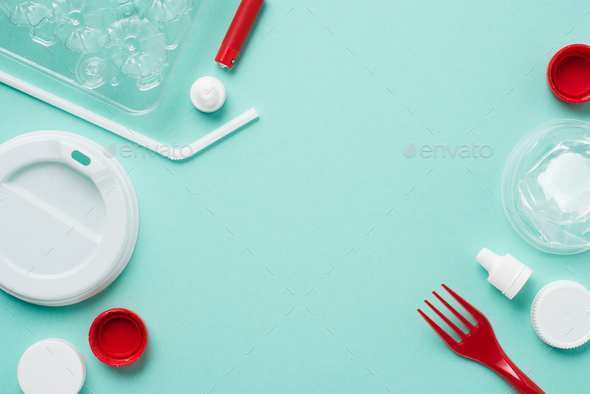 Top view of plastic bottle caps, drinking straw, fork, eggs tray and lid on blue background