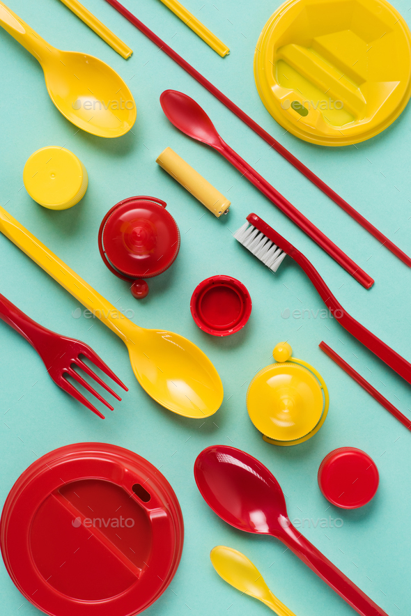 Flat lay with red and yellow disposable plastic wares arranged on blue background