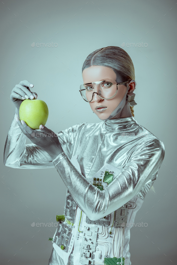 robot in futuristic eyeglasses holding apple and looking at camera isolated on grey, future