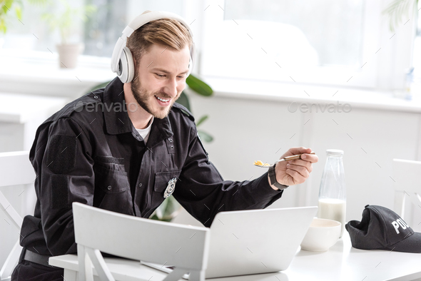 Handsome police officer having breakfast and listening to music with headphones at kitchen table