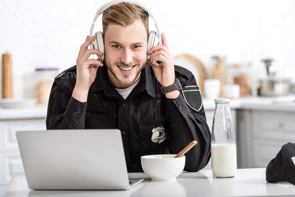 smiling police officer having breakfast and listening to music with headphones at kitchen table