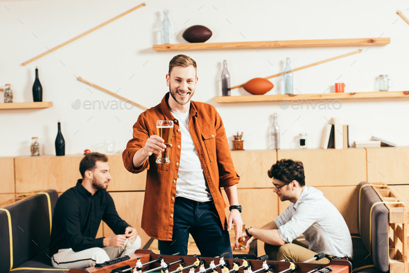 selective focus of smiling man with glass of beer standing at tablet football in cafe with friends