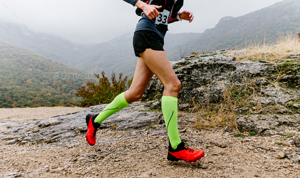 female athlete in compression socks running mountain trail race