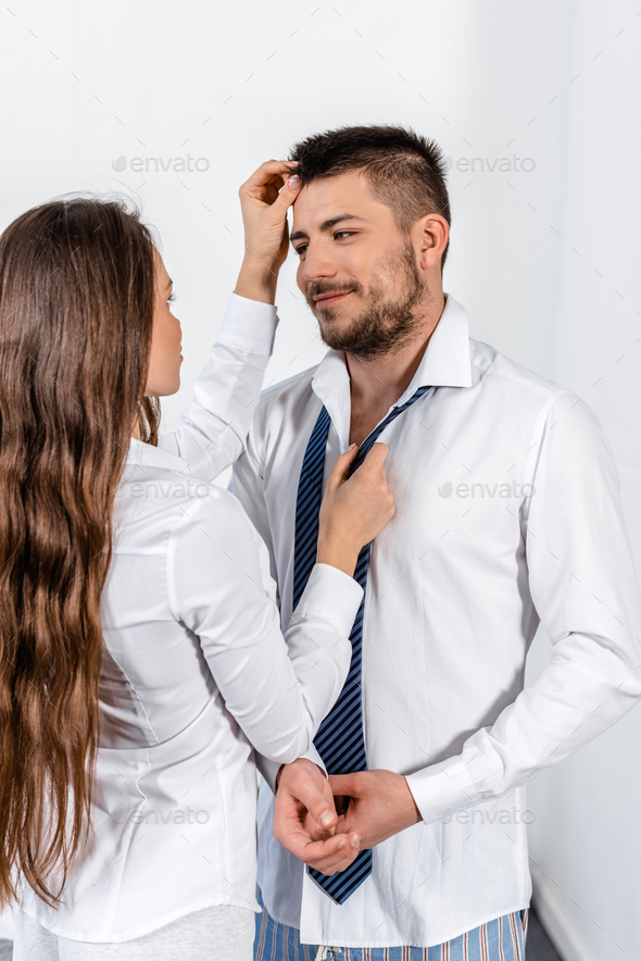 girlfriend tying boyfriend tie and touching his hair in morning on weekday in bedroom, social role