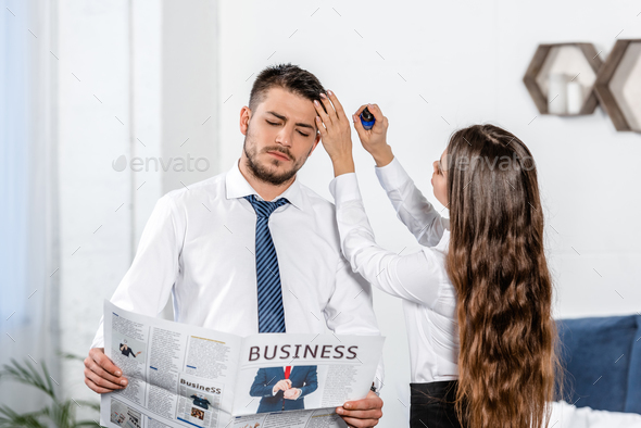 girlfriend styling boyfriend hair and he reading business newspaper at home, social role concept