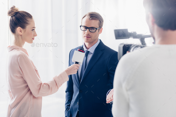 handsome businessman in glasses giving video interview to journalist in office